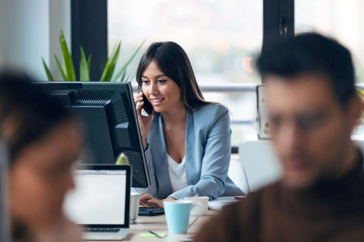 shot-smart-young-businesswoman-talking-with-mobile-phone-while-working-with-computer-modern-workspace