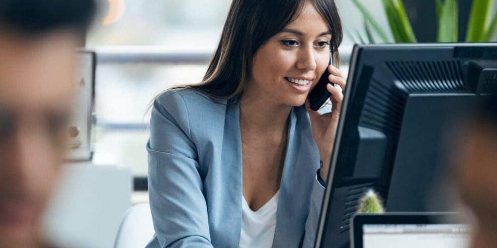 smart-young-businesswoman-talking-with-mobile-phone-while-working-with-computer-modern-workspace