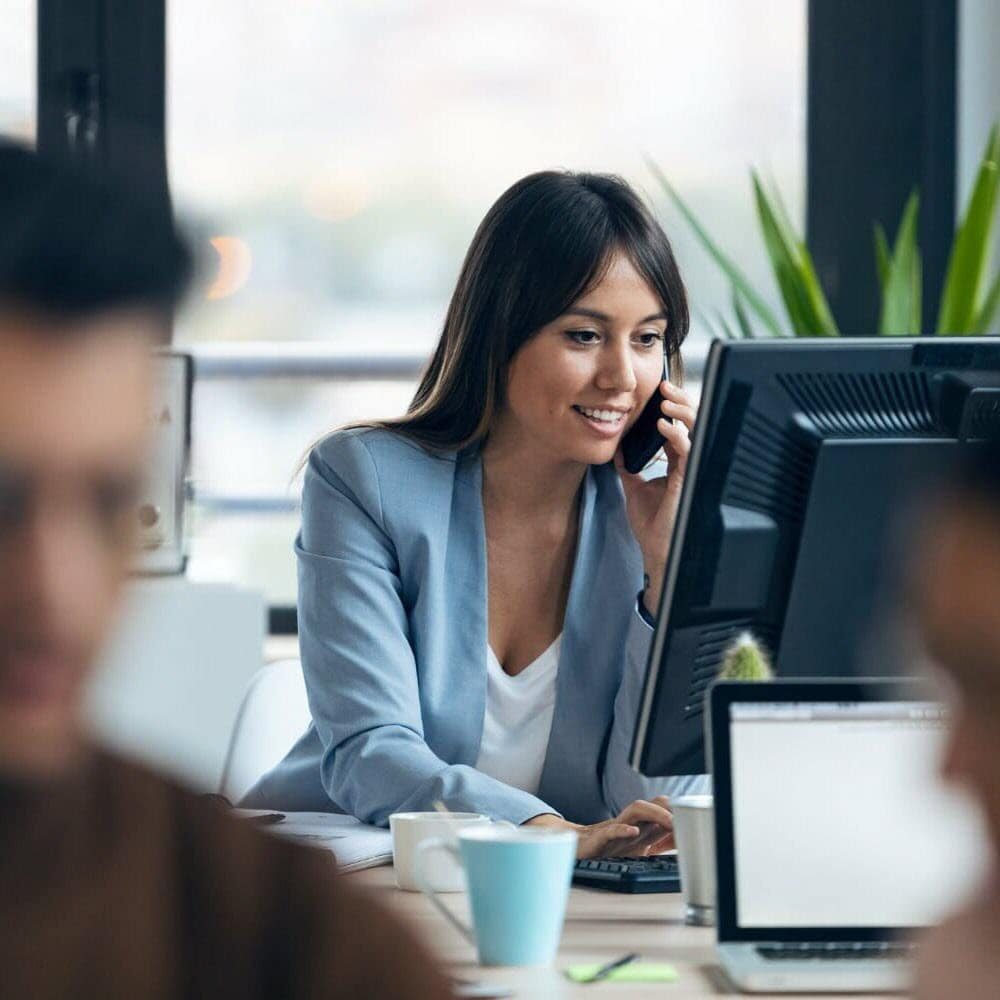 smart-young-businesswoman-talking-with-mobile-phone-while-working-with-computer-modern-workspace